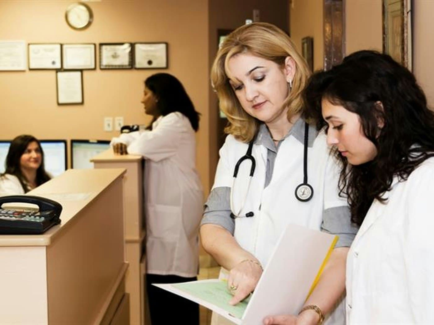 Two clinicians reviewing a patient file at a clinic front desk