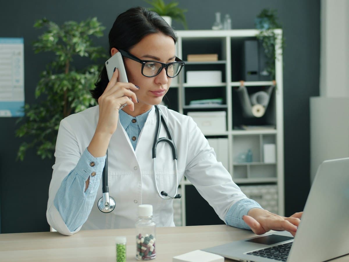 A clinician on the phone at her desk while working on a laptop
