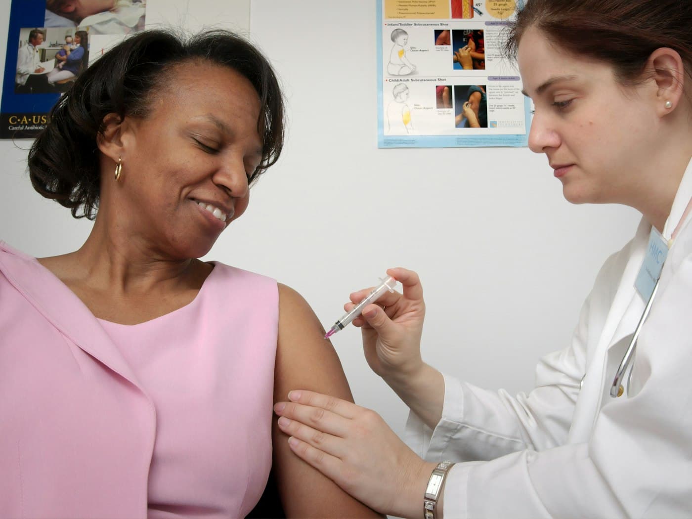 A clinician giving a smiling patient a vaccine in the upper arm